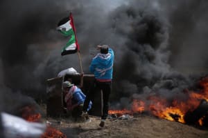A Palestinian youth throws a stone with a home-made sling through thick black smoke