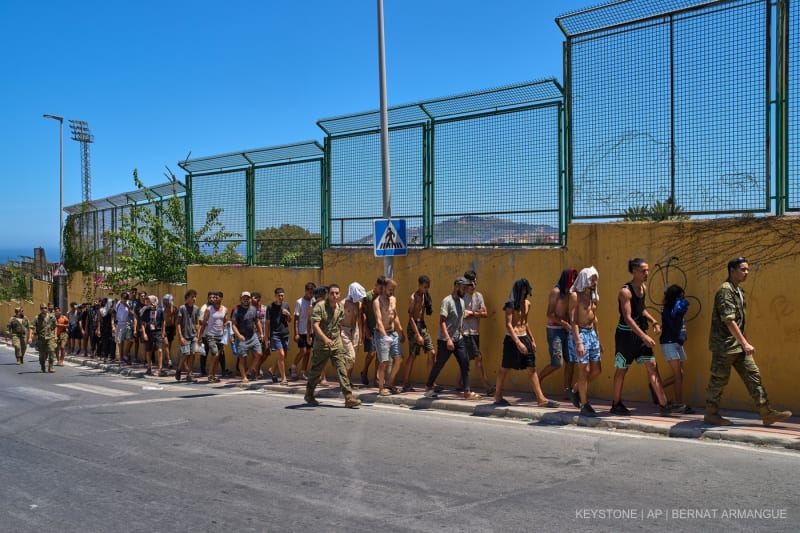 Migranten, die nach Spanien eingereist sind, werden am Sonntag, dem 2. August 2026, von spanischen Soldaten in Richtung der spanisch-marokkanischen Grenze begleitet, um von der spanischen Enklave Ceuta nach Marokko zurückgeführt zu werden.