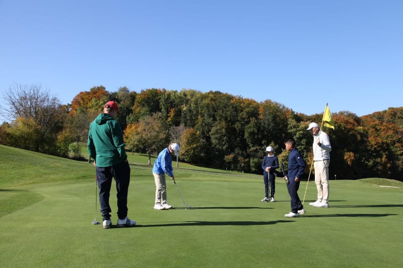 Sowohl Kinder als auch Erwachsene schauen zu, wie ein junger Golfer auf einem Golfplatz einen Putt spielt.