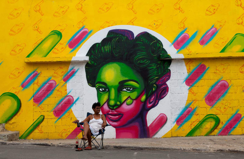 Eine Frau ruht sich auf einem Stuhl neben einem Grafitti im Viertel Santa Barbara in der Colnian Zone in Santo Domingo, Dominikanische Republik, aus.