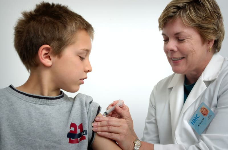 A nurse in the process of administering a vaccination in the shoulder of a young boy.