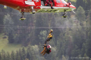 Ein Rega-Helikopter fliegt einen Retter und Bergungsmaterial vom Ungluecksort im Beriech der Kirche St. Peter Mistail, Hintergrund, zum Umladeplatz am Mittwoch, 13. August 2014, in Tiefenkastel.