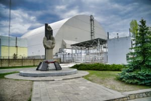 Monument to the victims of Chernobyl in front of the sarcophagus encapsulating reactor 4