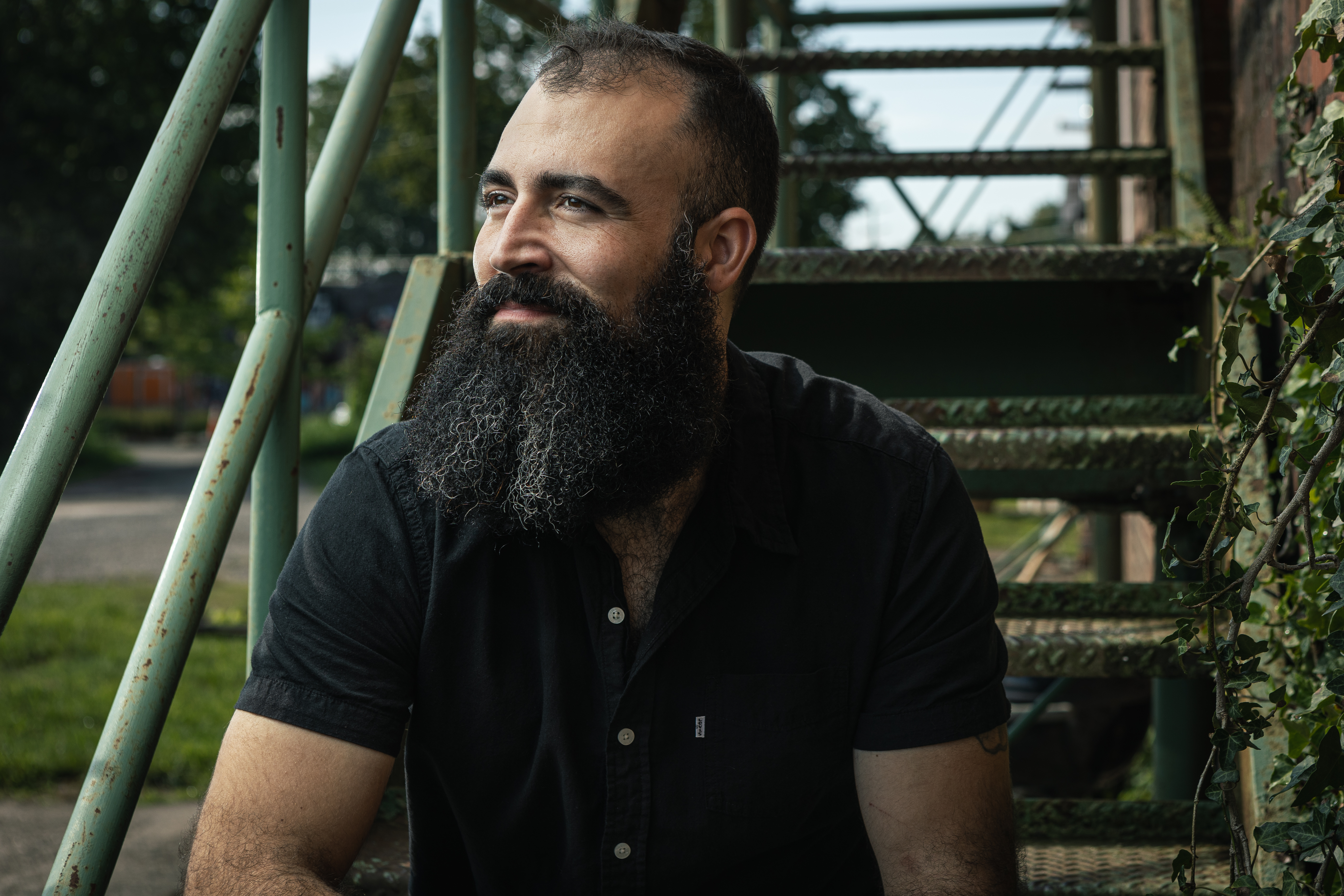 Headshot of man sitting on metal staircase looking off in the distance