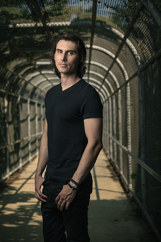 Young Man Wearing Black Shirt and pants standing inside a fenced in bridge near downtown Asheville