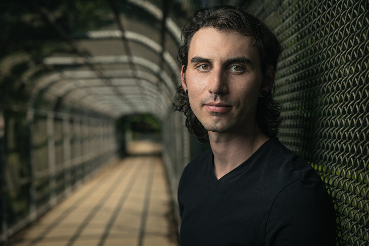 Young man standing on a bridge with a fence cage around it