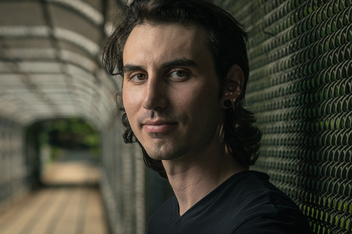 Environmental portrait of a male model in downtown Asheville standing on a bridge with a chainlink fence in the background. 