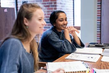 Two female students sitting at a desk taking notes in a class English for Corporate Communications
