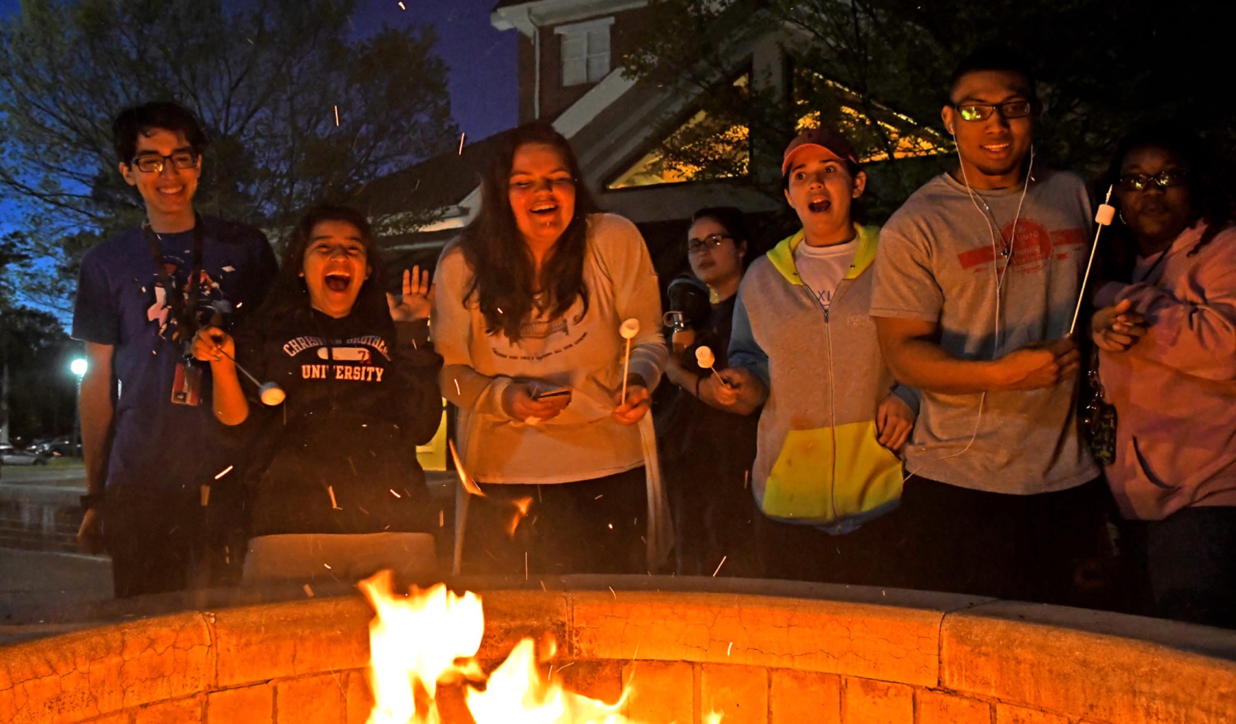 A group of CBU students standing around a fire at night roasting marshmallows