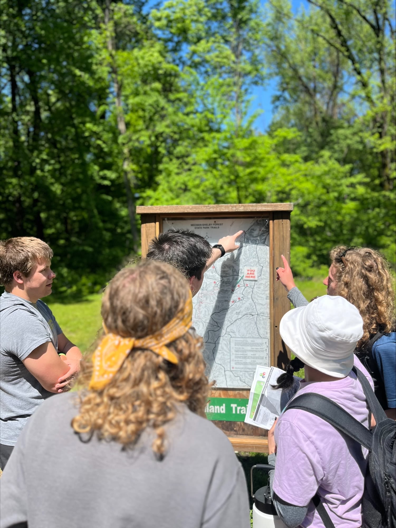 Four honors students outside on a nature trail looking at a map.