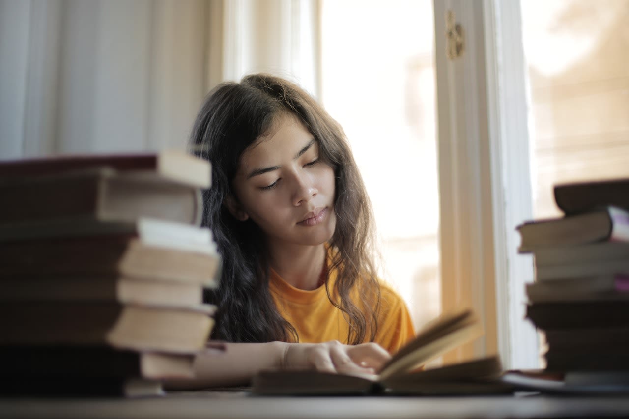 Girl sitting and reading at a desk surrounded by books