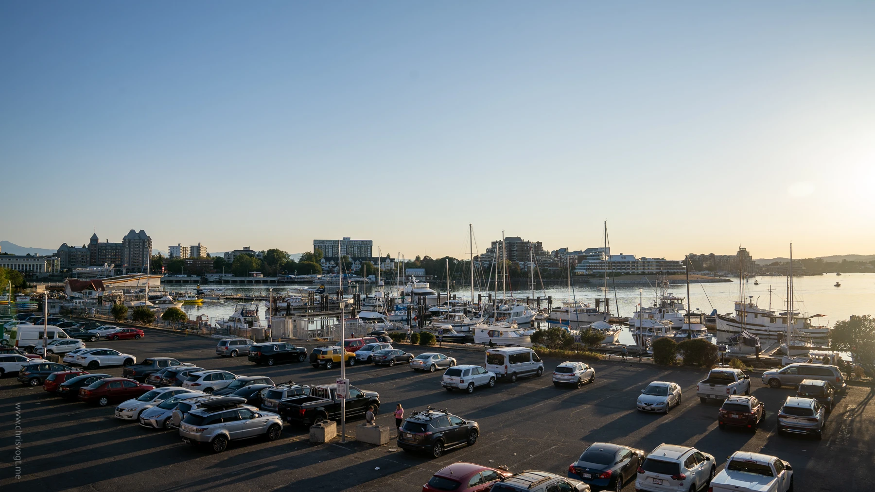 Boats docked in the harbor in Victoria, Canada as shadows reflect off cars parked on in a parking lot