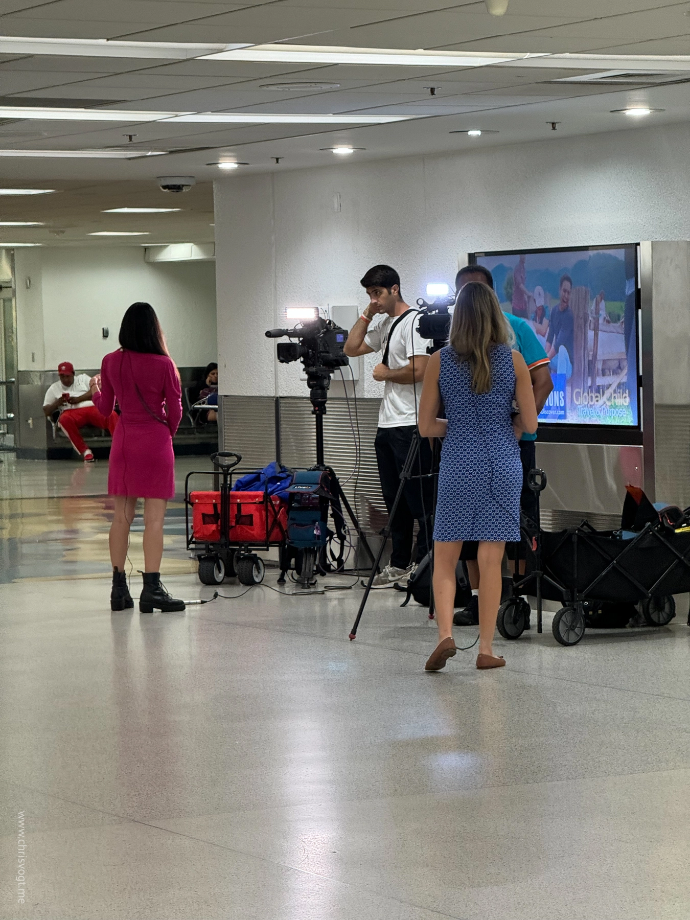 A news crew films passengers arriving at the baggage claim area in MIA.