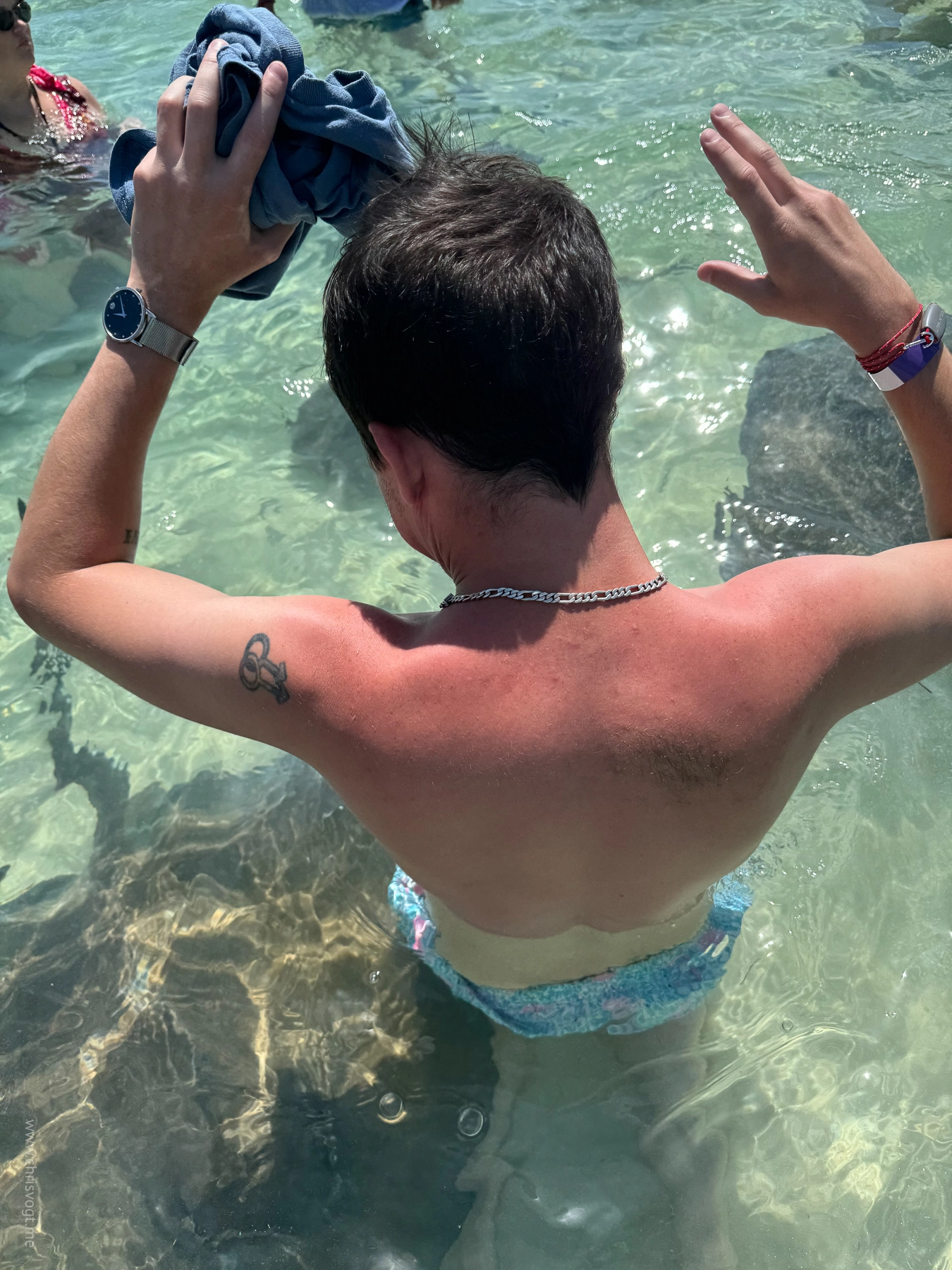 Nick holds his shirt out of the water as stingrays swim up to feel him in Bimini, Bahamas.