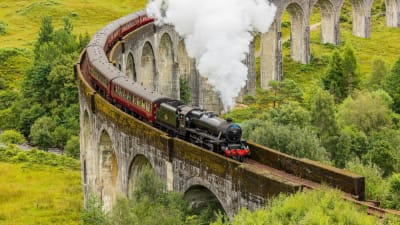 Famous 'Hogwarts Express' steam training passing over a curved viaduct in the Scottish Highlands.png