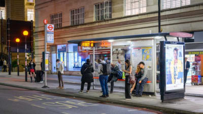 People Waiting At A London Bus Stop At Night Time.
