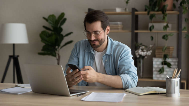 Junger Mann, der auf seinem Handy am Schreibtisch tippt