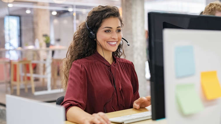 Frau sitzt am Arbeitsplatz und telefoniert über ihr Headset