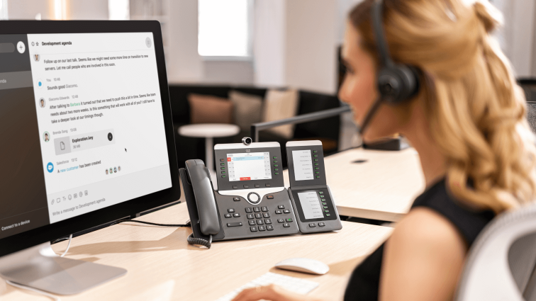 Frau, die per Headset am Schreibtisch mit einem Business-Telefon telefoniert