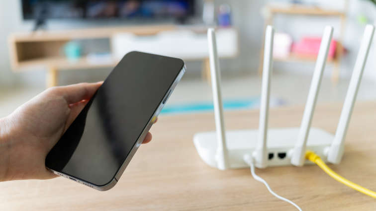 Mann der mit seinem Handy nebem dem DSL-Router steht