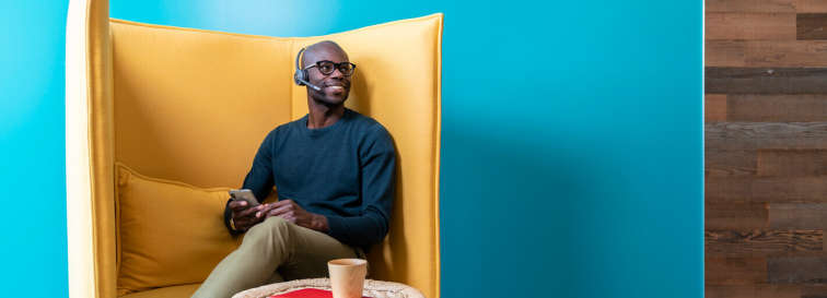 Mann telefoniert in einem Sessel entspannt per Headset über das Mobiltelefon