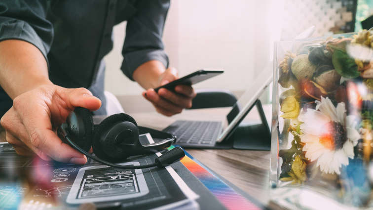 Mann am Laptop mit Smartphone und Headset