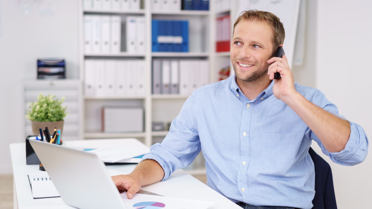 Mann, der an seinem Arbeitsplatz im Büro am Telefonieren ist