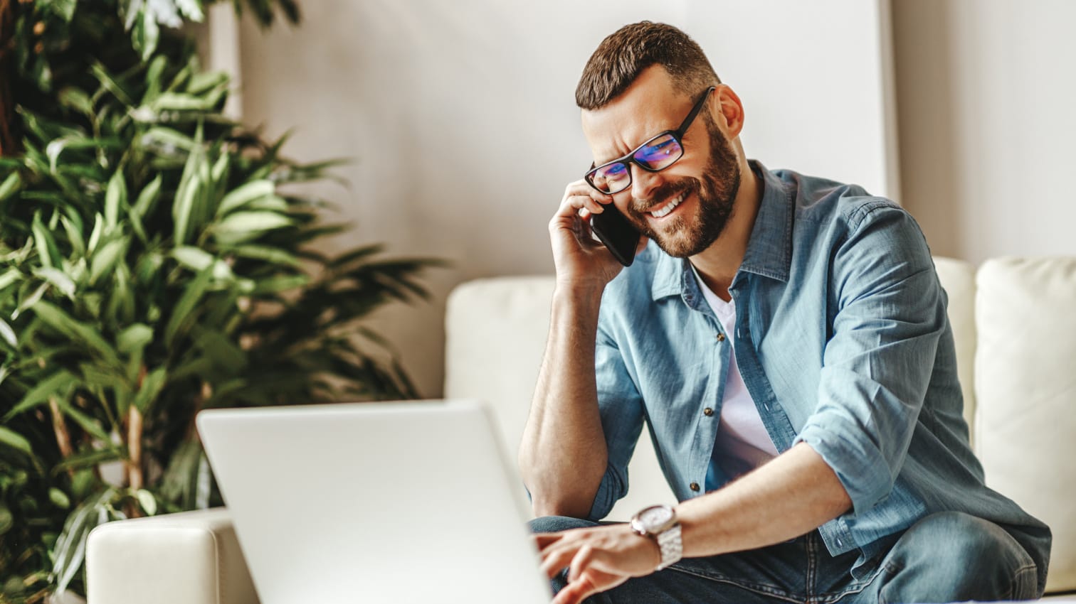 Mann telefoniert per Smartphone und arbeitet gleichzeitig am Laptop.