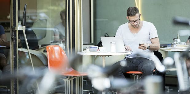 Ein Mann, der im Café arbeitet und auch mobil über den PC und das Handy dank Softphone erreichbar ist.