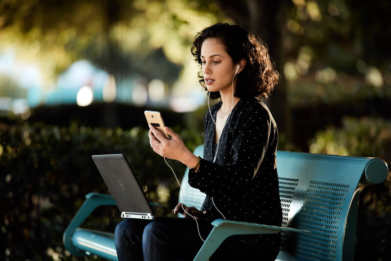 Eine Frau arbeitet mobil mit dem Handy und dem Laptop im Park