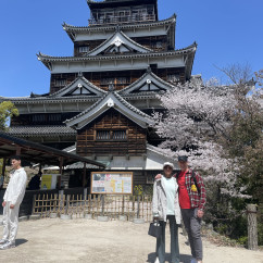 People stand in front of Hiroshima Castle with cherry blossom trees in the background.