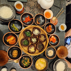 Korean banchan dishes arranged on a gray stone table with rice and tea.