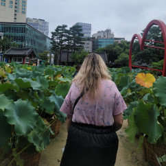 Back view of a person surrounded by lush greenery and urban architecture.