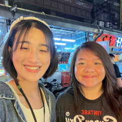 People taking a selfie in front of a shop display with neon signs.