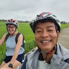 Man and woman cycling on a path with green fields surrounding them.