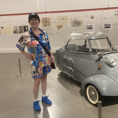 Woman in colorful attire beside a microcar display indoors.