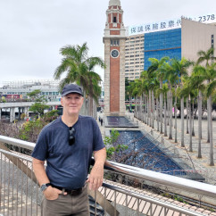 Man standing in front of Tsim Sha Tsui Clock Tower in Hong Kong.