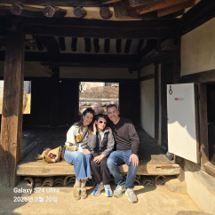 Three people sitting on a wooden platform in a traditional Korean house.
