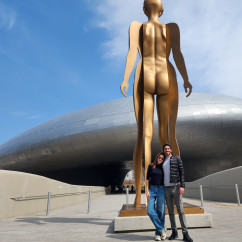 Two people stand in front of a large golden sculpture at Dongdaemun Design Plaza.
