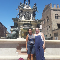 Bright smiles beneath Bologna's striking Neptune Fountain under a clear sky.