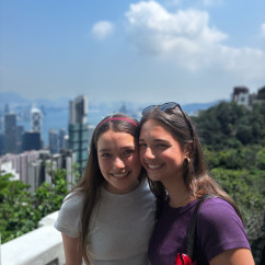 Two friends share a smile with Hong Kong's skyscrapers behind them.