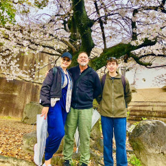A group smiles beneath blooming cherry blossoms in Osaka.