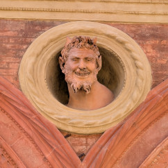 A mischievous stone face peers from Bologna's intricate brickwork.