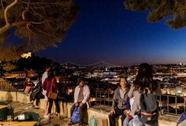 Locals and tourists sitting at a viewpoint after sunset in Lisbon