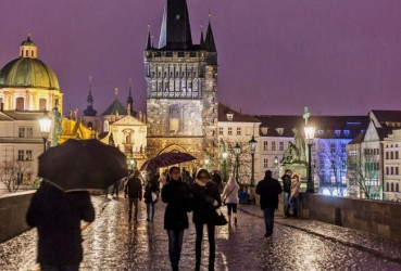 Tourists walking along Charles Bridge on a rainy evening in Prague