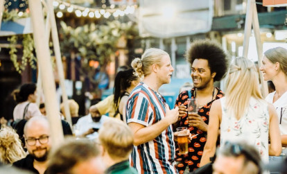 Tourists enjoying drinks with a local at a trendy night market in London