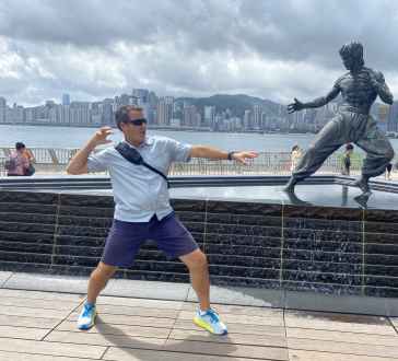 Playfully mimicking the statue's pose on a cloudy Hong Kong day.