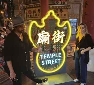 Neon sign reading 'Temple Street' with two people posing beside it in Hong Kong.