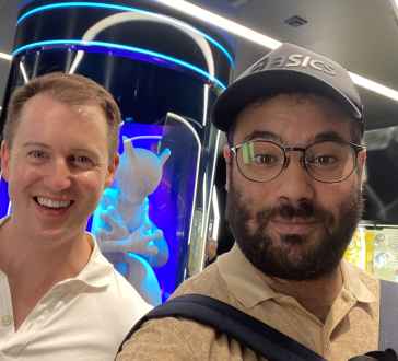 Individuals in a technologically themed room with curved glass and neon lights.