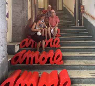 People sitting on red 'amore' benches on a marble staircase.